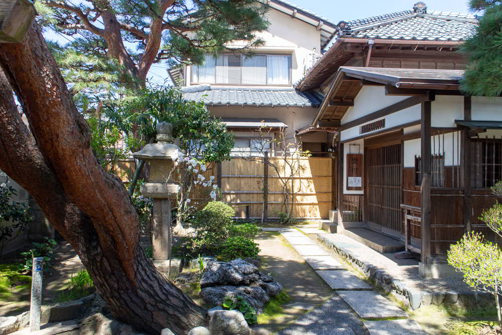 Ein Hinterhof mit Pflaumenbaum im Vordergrund und traditionellen japanischen Häusern in Niigata.