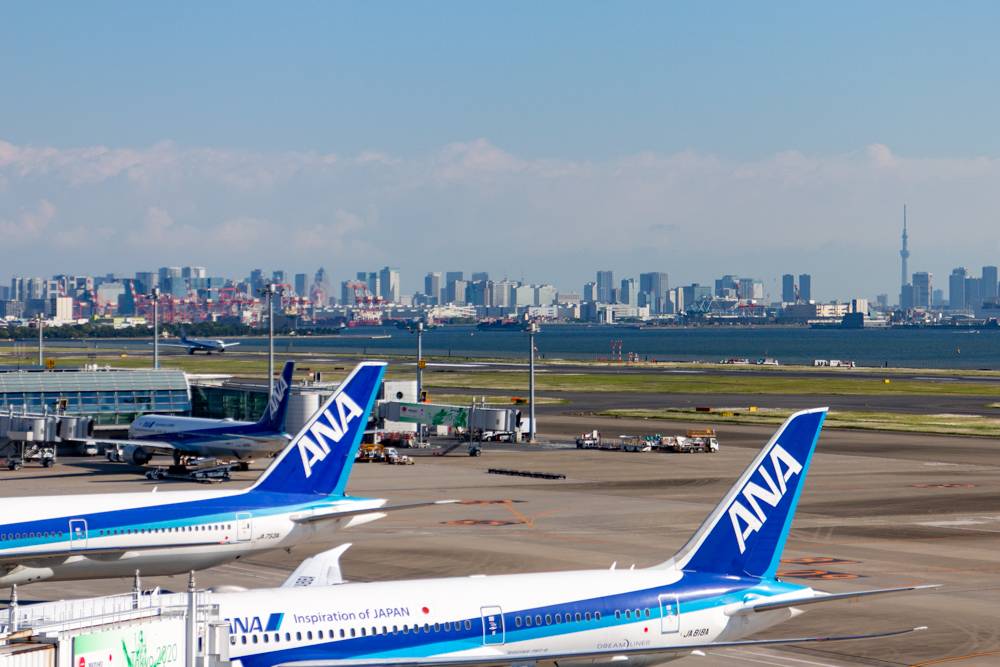 Los geht die Reise am Terminal 2 am Flughafen Haneda in Tokyo: ANA Flugzeuge am Terminal mit der Skyline Tokyos und dem Sky-Tree im Hintergrund.