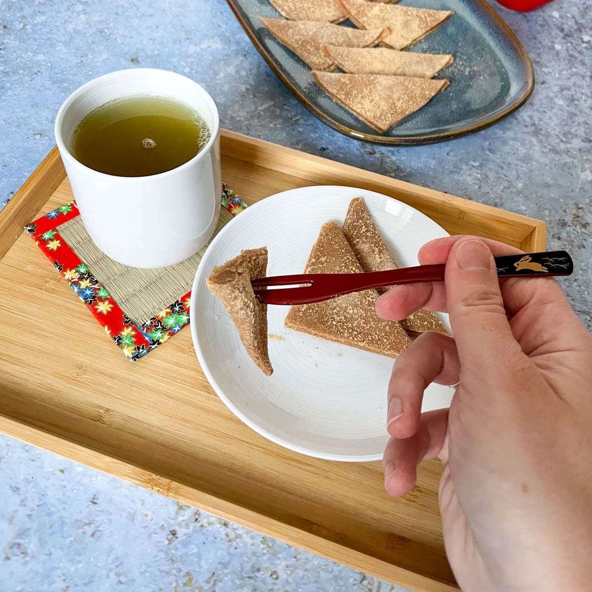 Yatsuhashi auf Holzatablet und mit japanischer Wagashi-Gabel. Dazu ein grüner Tee