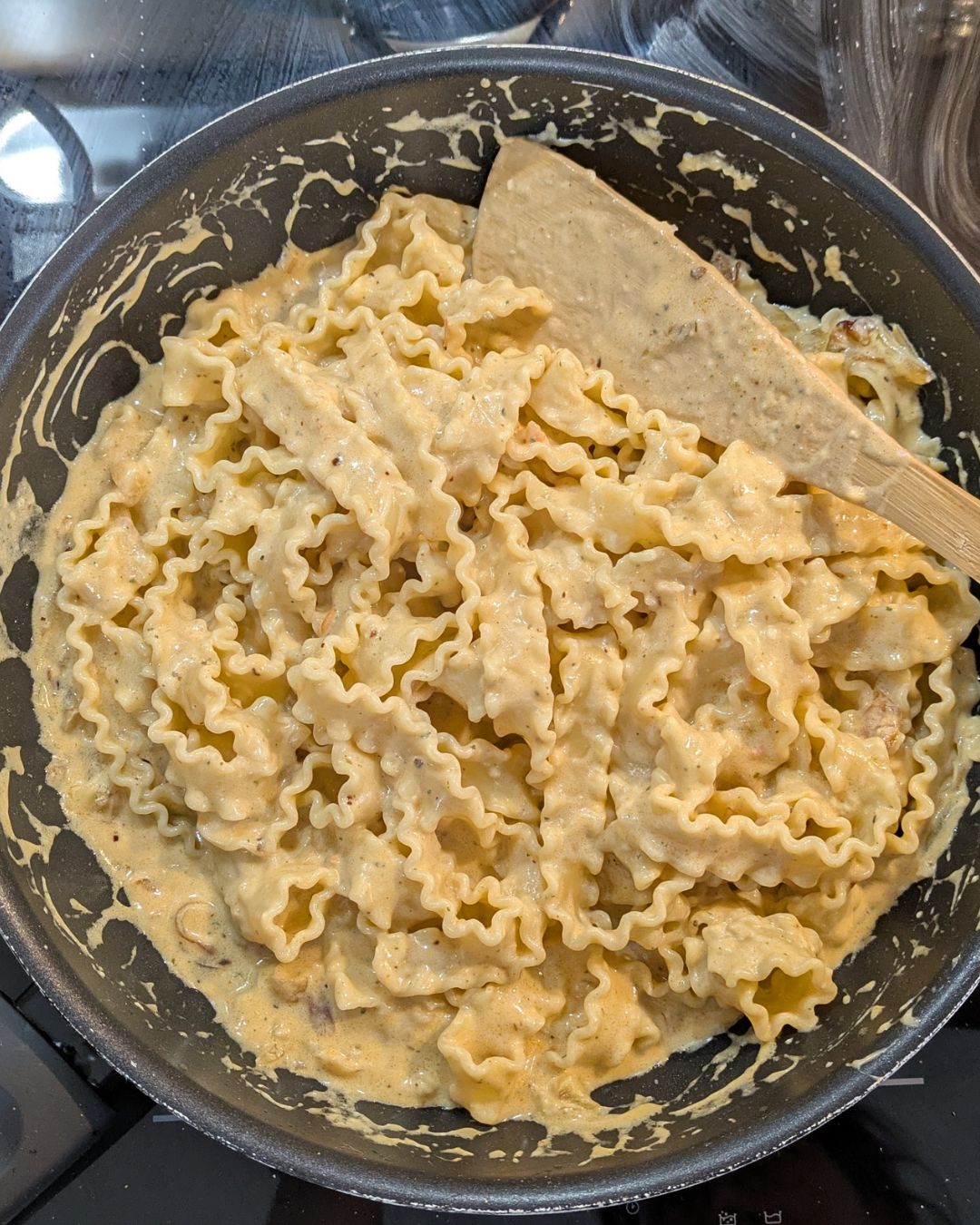 ange Wellennudeln (Mafaldine), die vollständig von der cremigen, hellbraunen Zwiebel-Rayu-Sauce in der Pfanne umhüllt sind.