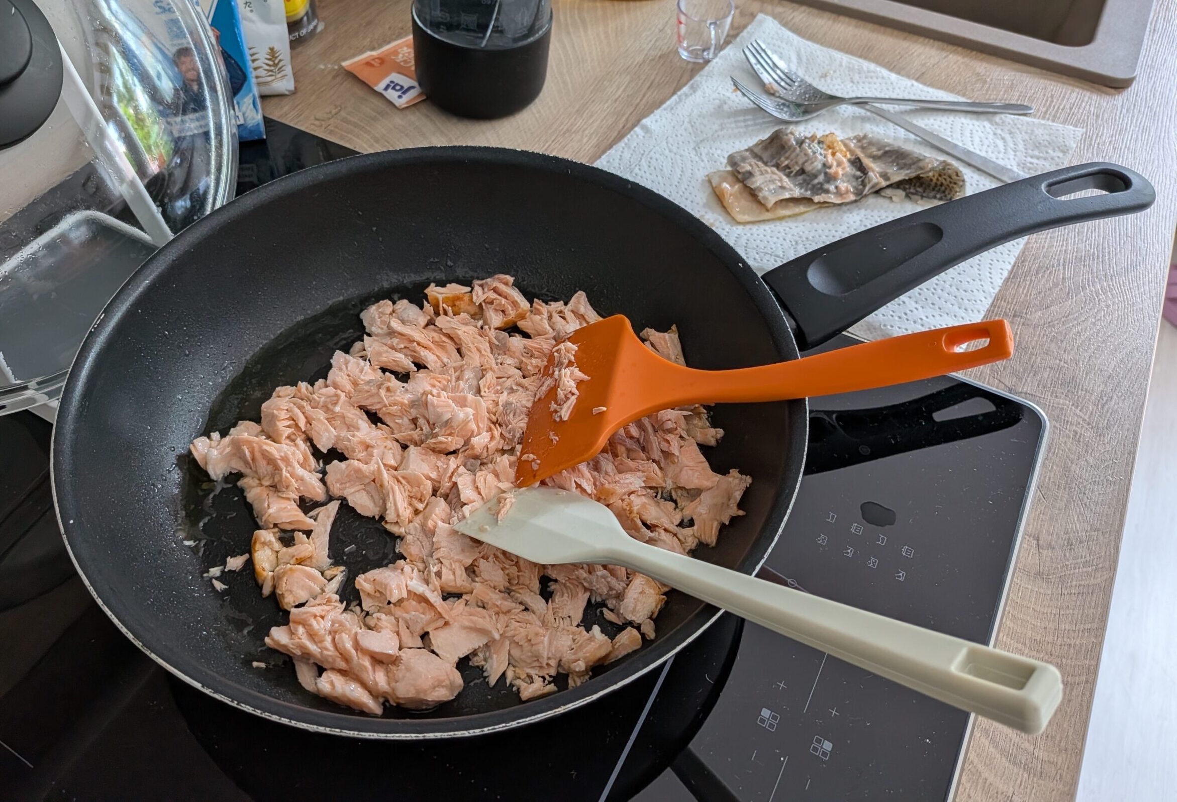 Eine nähere Ansicht der Lachsflocken, die in der Pfanne mit dem orangen Pfannenwender zerkleinert und gemischt werden.